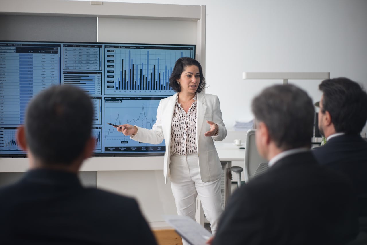 why-choose-us-02 Professional woman presenting stock market data in a modern office setting.